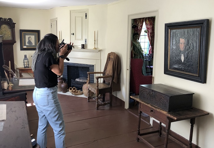 A Public Humanities and Heritage student is taking photos of a painting and artifacts in a museum.