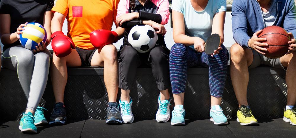 People sitting in athletic gear holding different sports equipment
