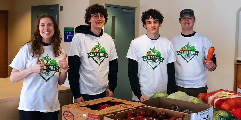 Four students in Square Roots T-shorts stand in front of vegetables. One student gives a thumbs up.