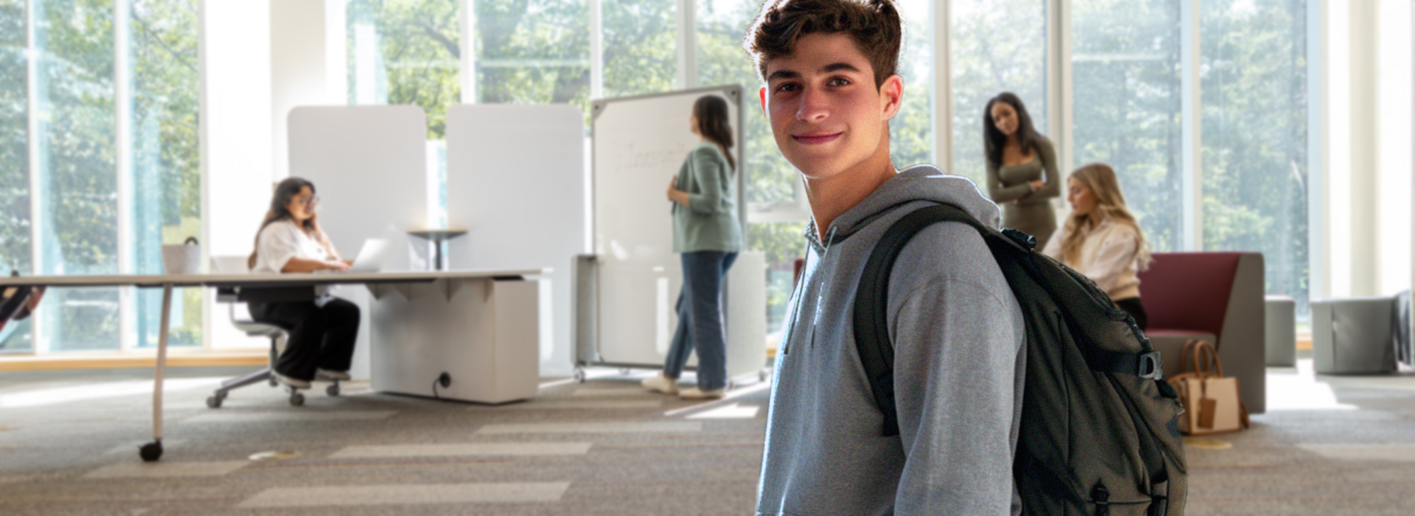 A young man with a backpack is walking by some cubicles.