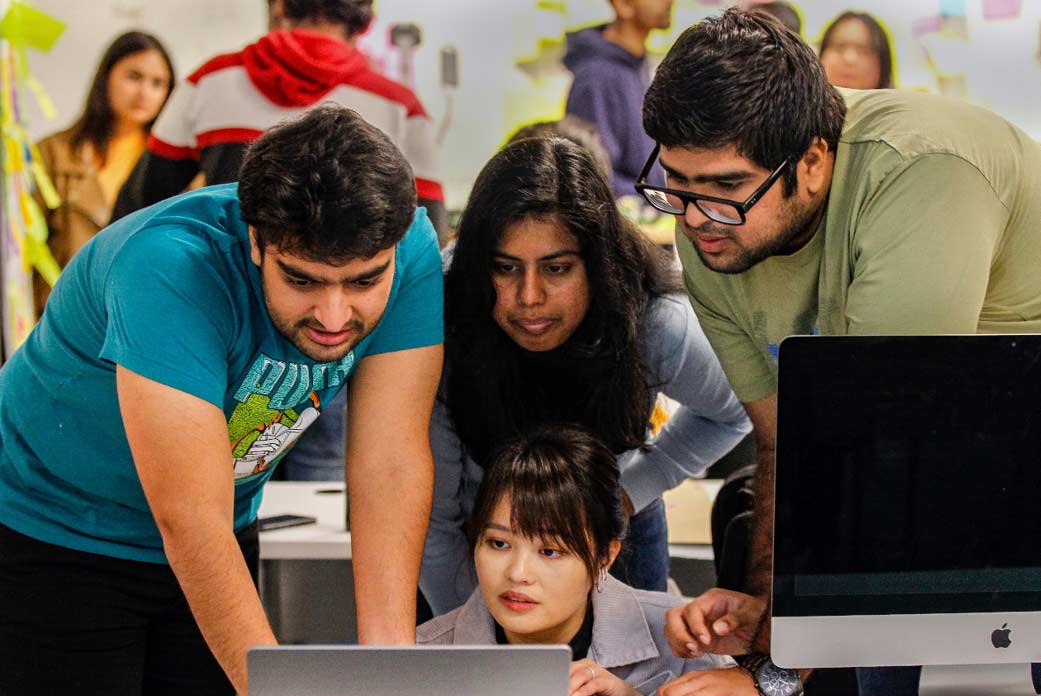 Group of four international students viewing a computer screen.